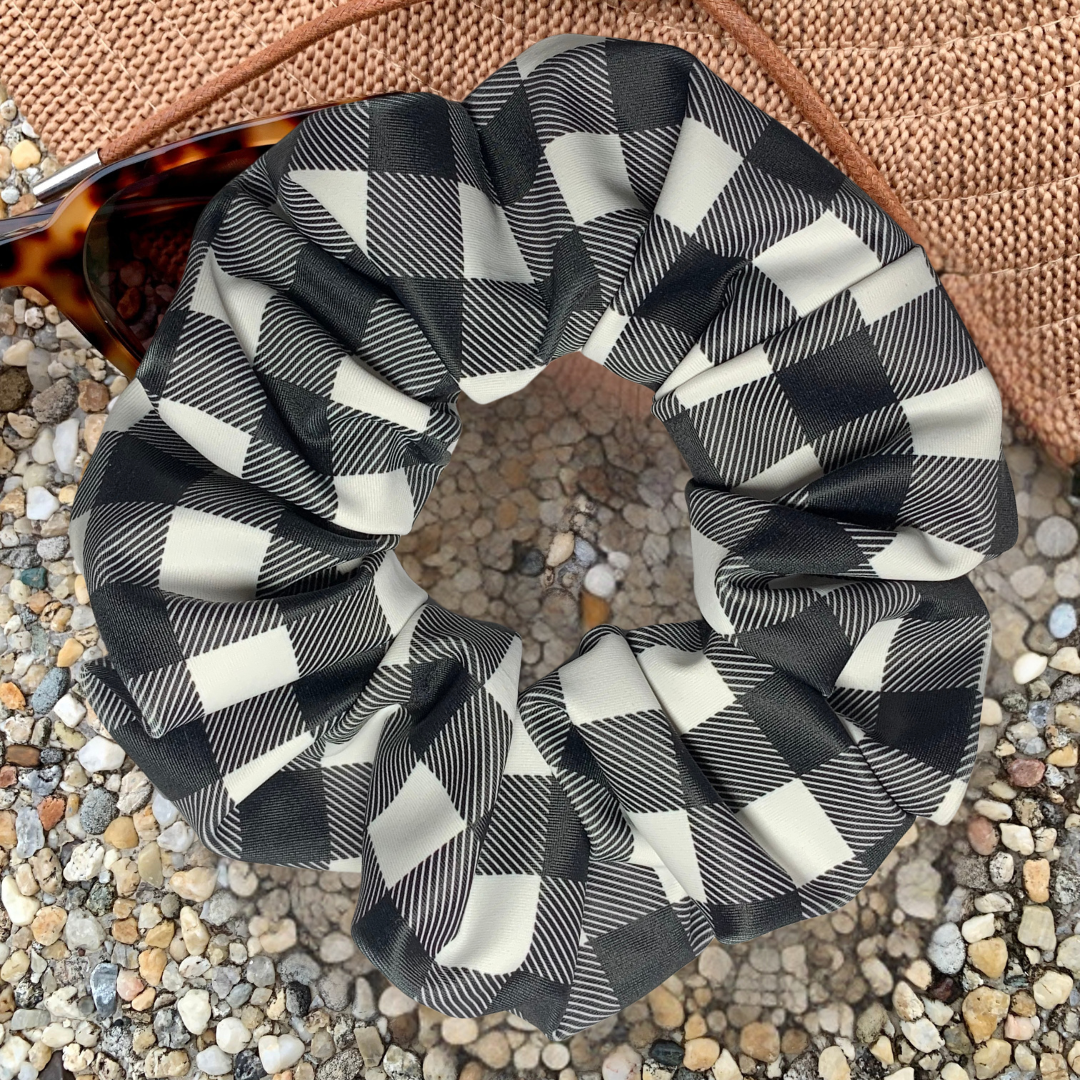 Black and white checkered swim scrunchie on a textured surface with hat and sunglasses