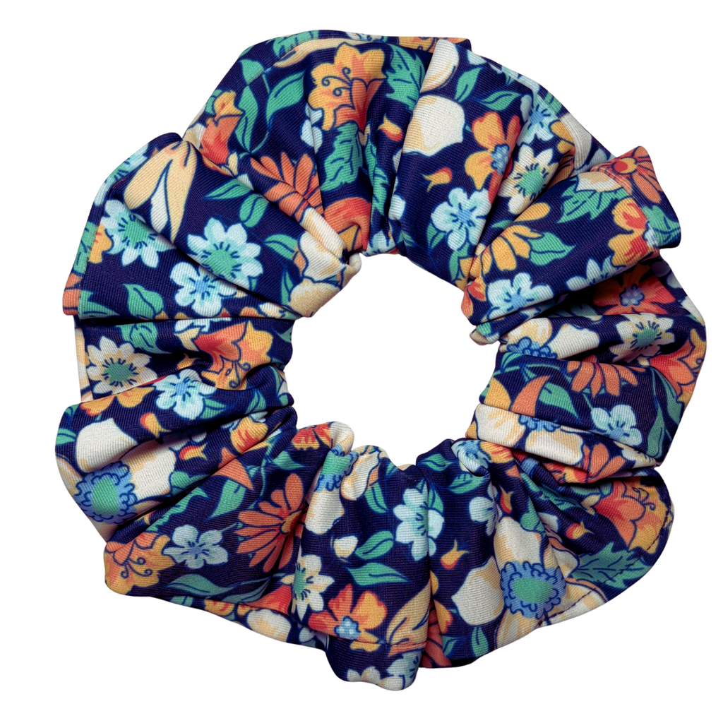 A fabric hair scrunchie with a colorful floral print on a dark navy blue background, featuring orange, light blue, green, and cream flowers.