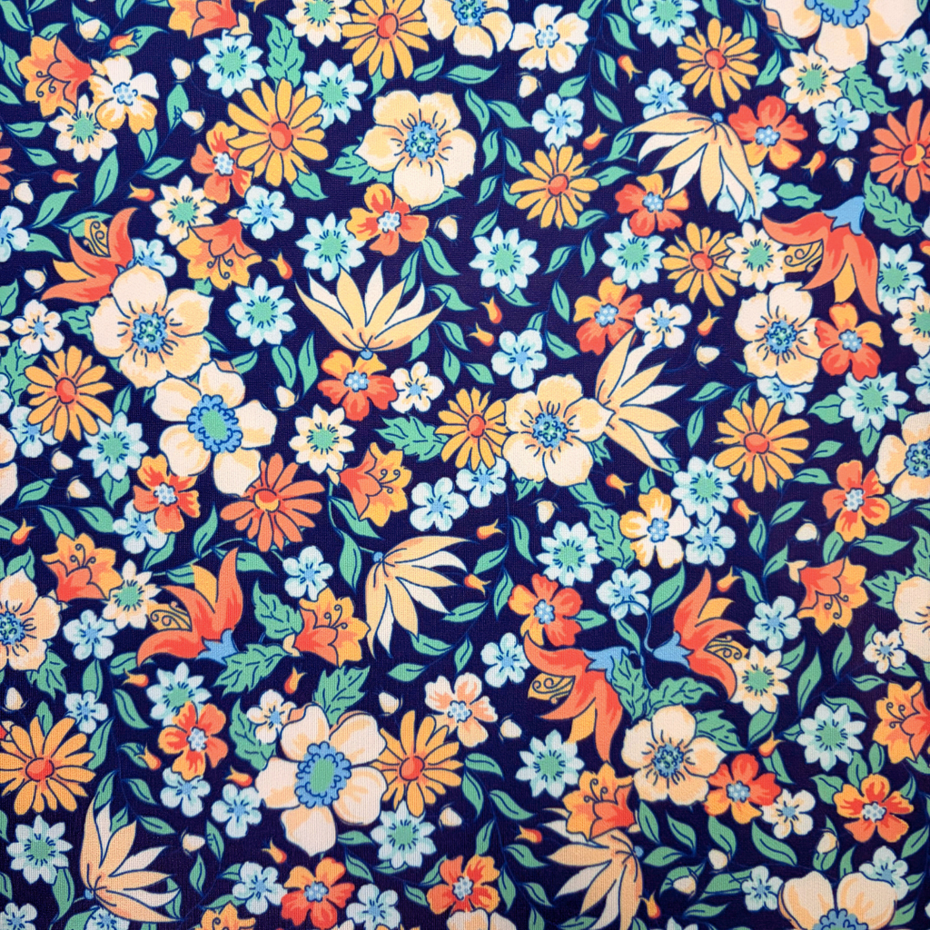 A close-up of a dense floral pattern featuring orange, yellow, light blue, and white flowers with green leaves on a dark navy blue background.