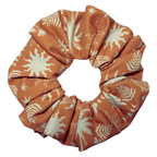 An orange fabric hair scrunchie with a white palm tree and sunburst pattern, shown on a solid white background.
