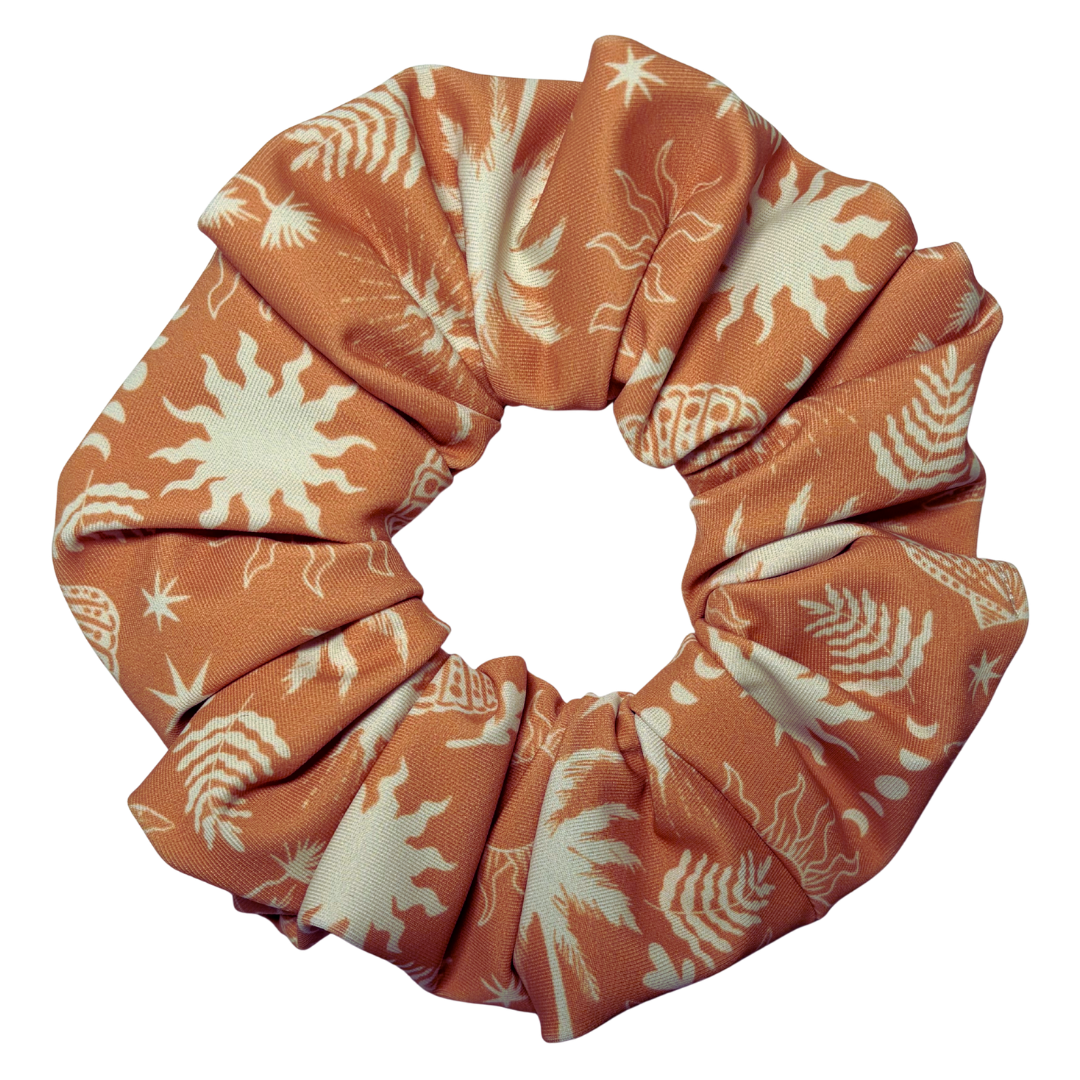 An orange fabric hair scrunchie with a white palm tree and sunburst pattern, shown on a solid white background.
