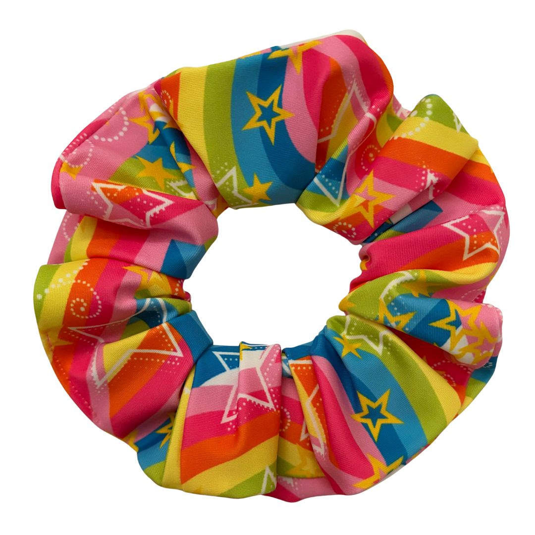 A fabric hair scrunchie featuring a vibrant multicolor pattern of pink, yellow, green, and blue stripes with yellow stars, set against a plain white background.