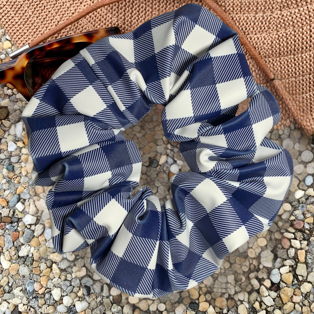 Blue and white checkered swim scrunchie on a textured surface with hat and sunglasses