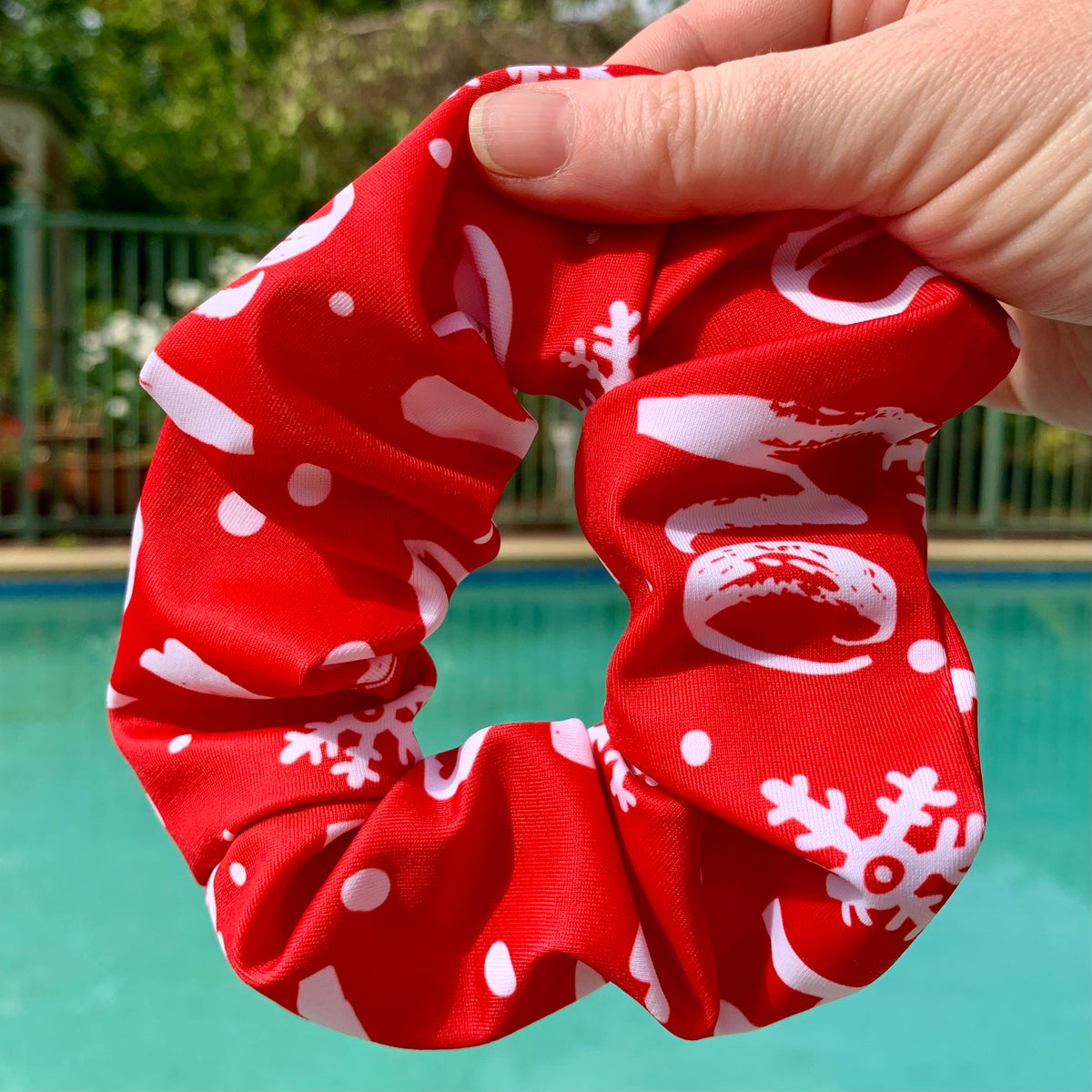Christmas Red swim scrunchie with white ho ho ho held in front of a pool with garden in background
