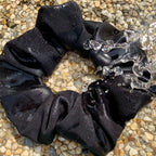 black swim scrunchie on pebble surface with water splashing on scrunchie
