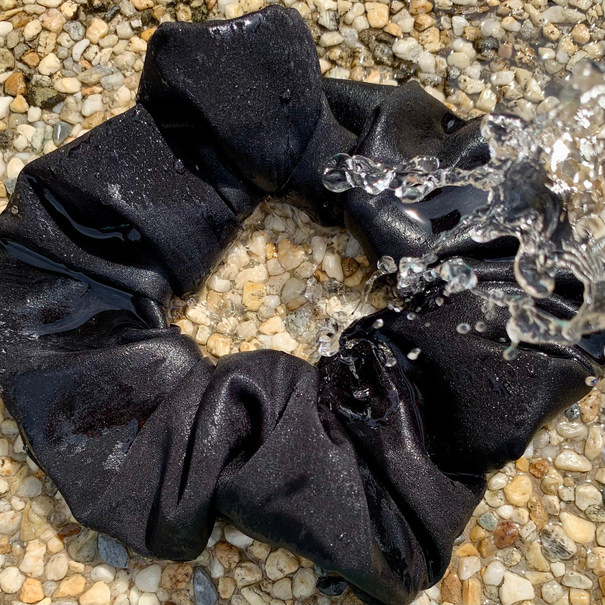 black swim scrunchie on pebble surface with water splashing on scrunchie