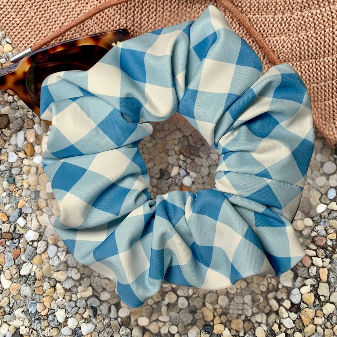 Blue and white checkered swim scrunchie on a textured surface with a hat and sunglasses