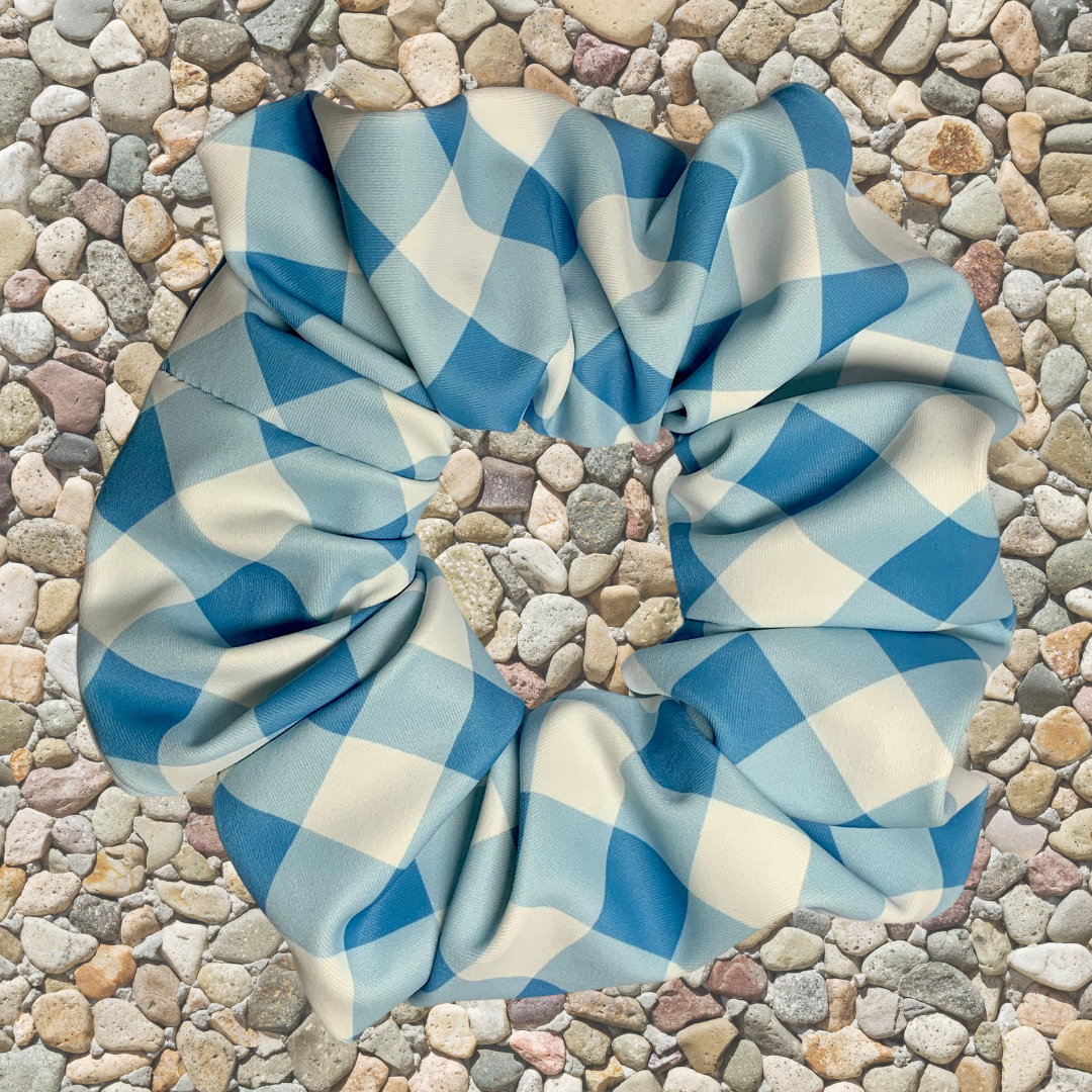 Blue and white checkered swim scrunchie on a pebbled surface