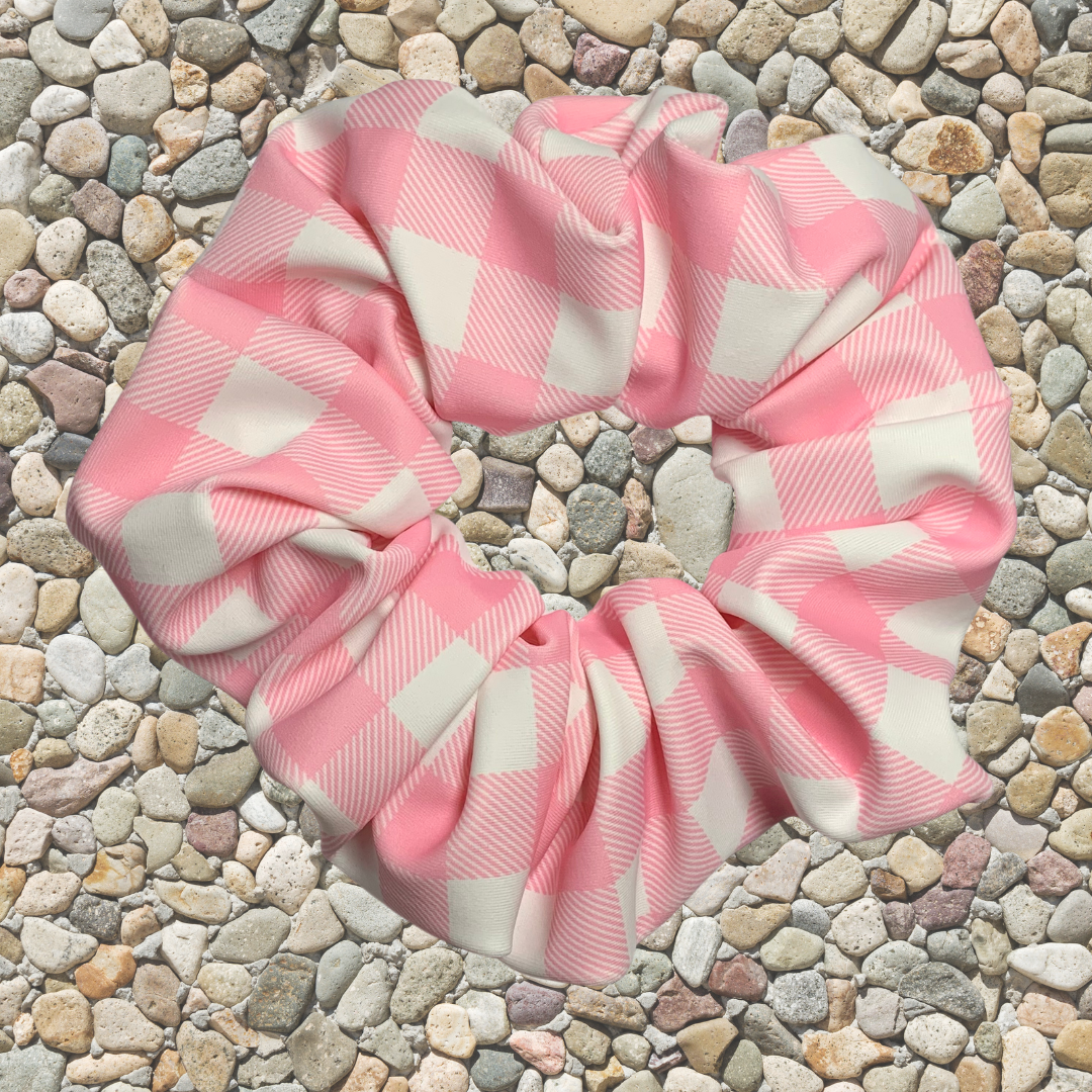 Pink and white checkered swim scrunchie on a pebbled surface