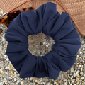 Navy blue scrunchie on a textured surface with sunglasses in the background
