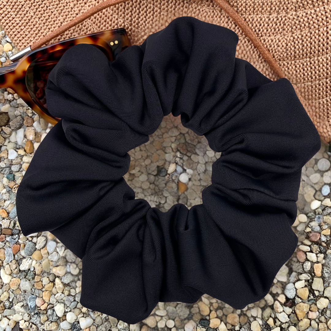 Black scrunchie on a textured surface with sunglasses in the background