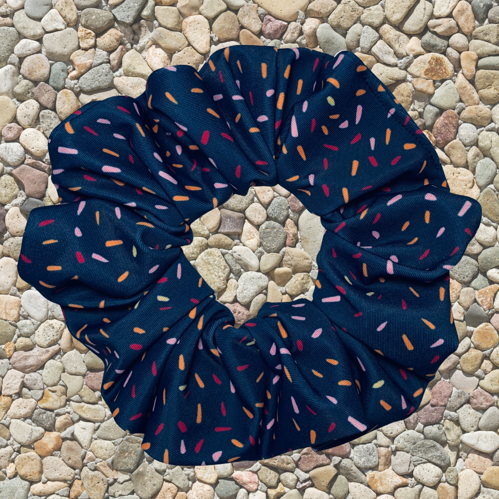 Navy blue scrunchie with colorful sprinkles on a pebble background