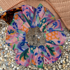 Colourful floral swim scrunchie on a textured surface with a hat and sunglasses
