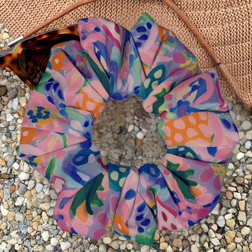 Colourful floral swim scrunchie on a textured surface with a hat and sunglasses
