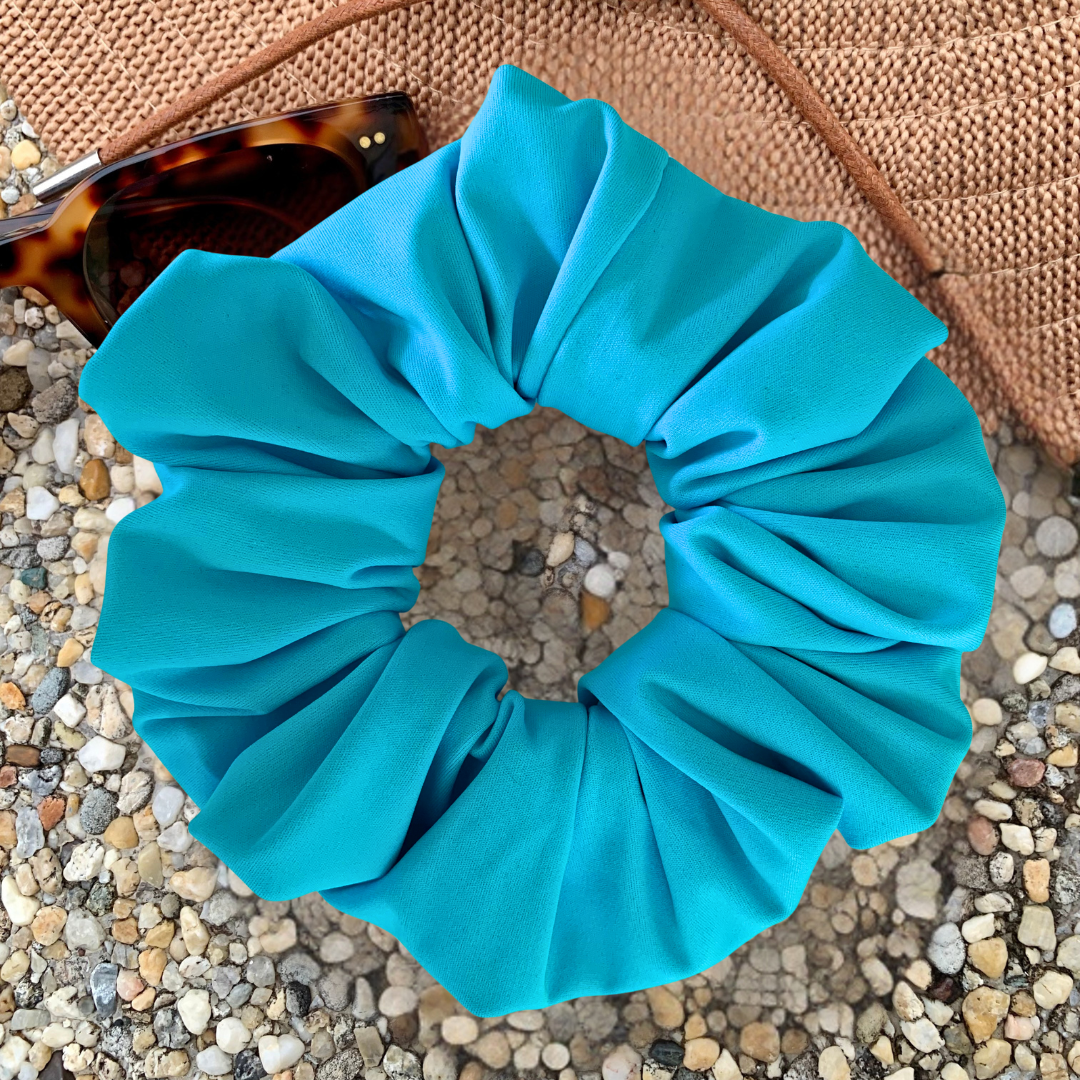 Blue scrunchie on a textured surface with sunglasses in the background