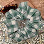 Green and white checkered swim scrunchie on a textured surface with sunglasses in the background