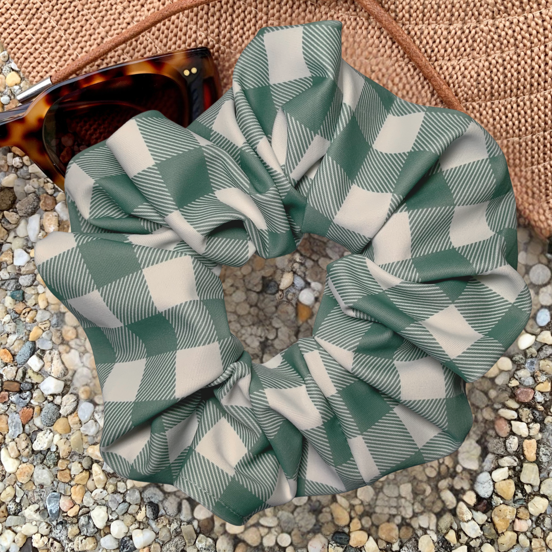 Green and white checkered swim scrunchie on a textured surface with sunglasses in the background