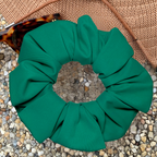 Green swim scrunchie on a textured surface with sunglasses