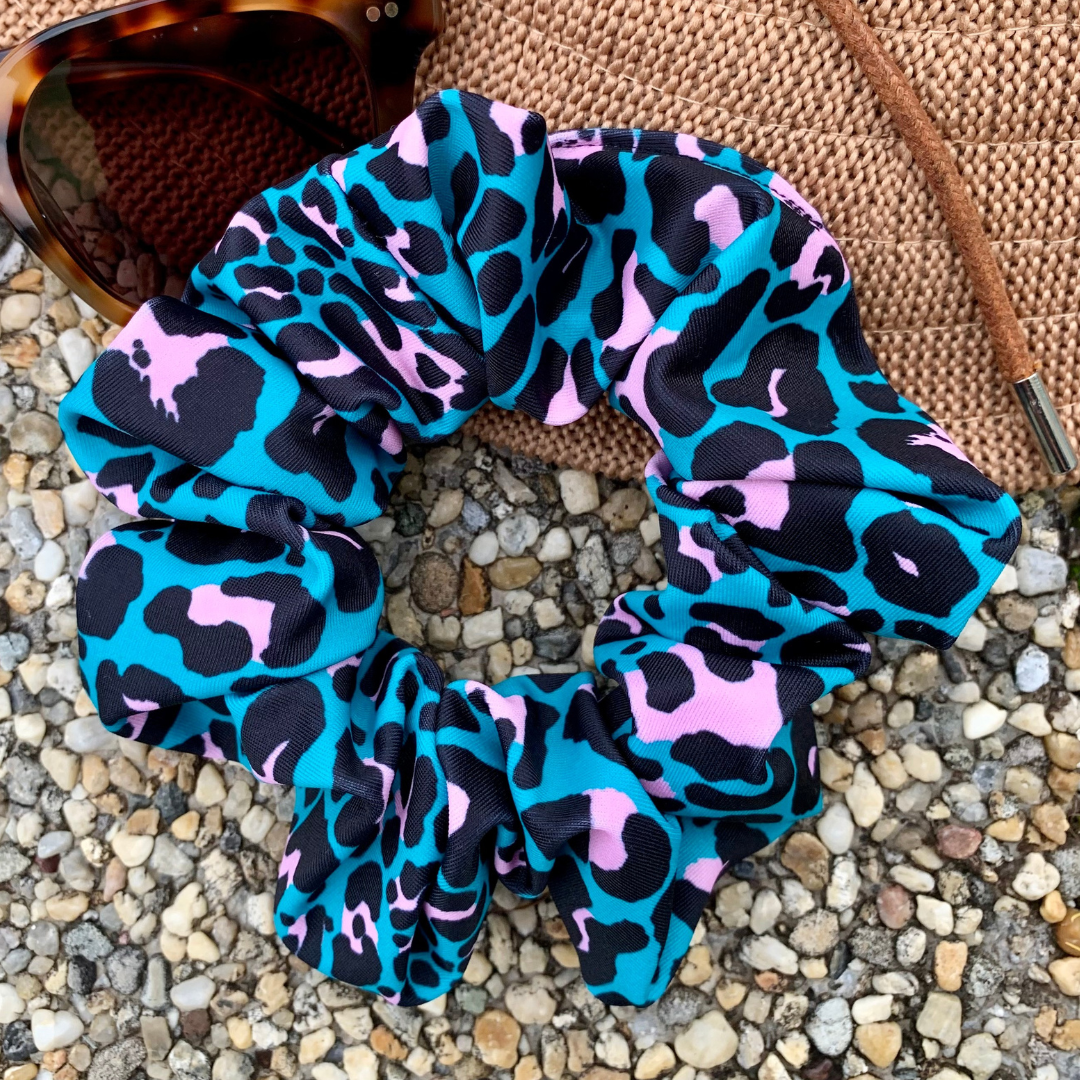Leopard print swim scrunchie with blue, black, and pink pattern on a textured surface.