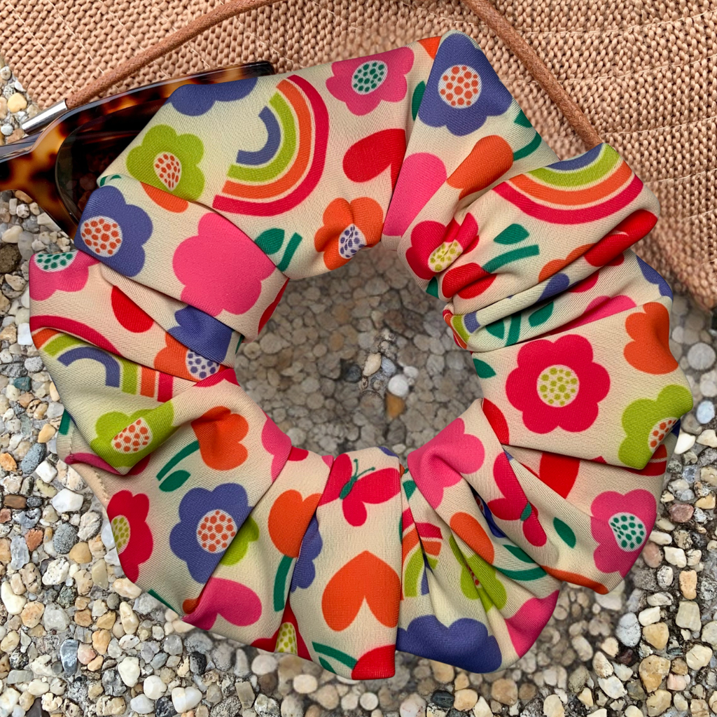 Colourful floral and heart patterned swim scrunchie on a textured surface