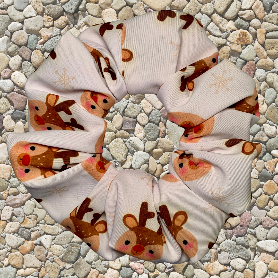 White fabric with reindeer pattern swim scrunchie on a pebble background
