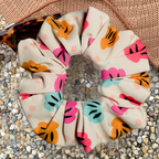 Swim scrunchie with colourful shell pattern on a textured surface with a hat and sunglasses