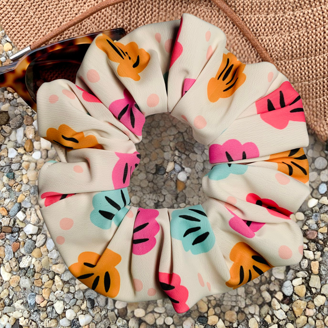 Swim scrunchie with colourful shell pattern on a textured surface with a hat and sunglasses