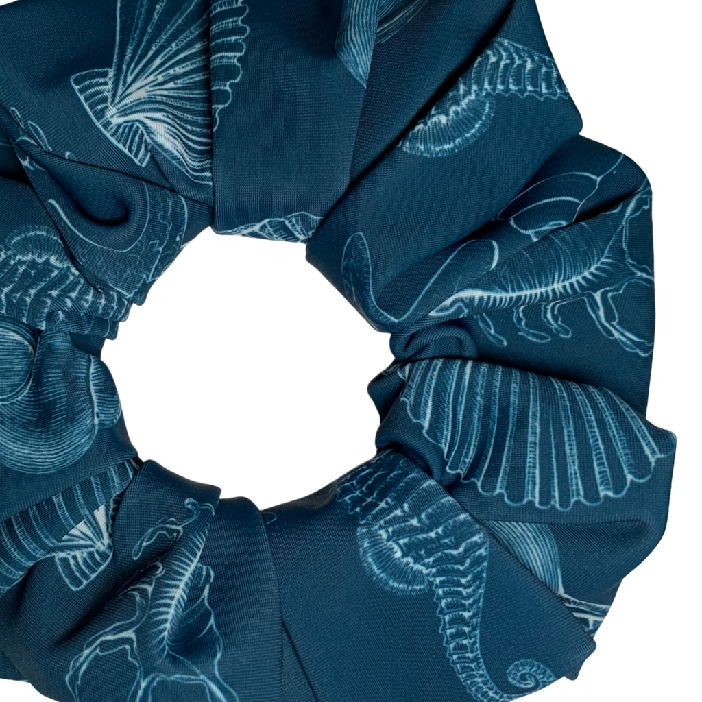 Close up of a blue swim scrunchie with white patterns of sea life and shells on a white background