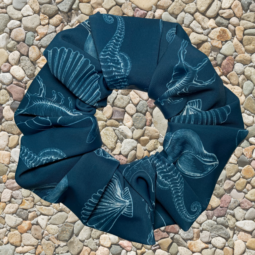 Blue swim scrunchie with white patterns of sea life and shells on a stone surface
