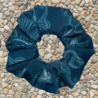 Blue swim scrunchie with white patterns of sea life and shells on a stone surface
