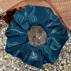 Blue swim scrunchie with white patterns of sea life and shells on a textured surface with hat and sunglasses