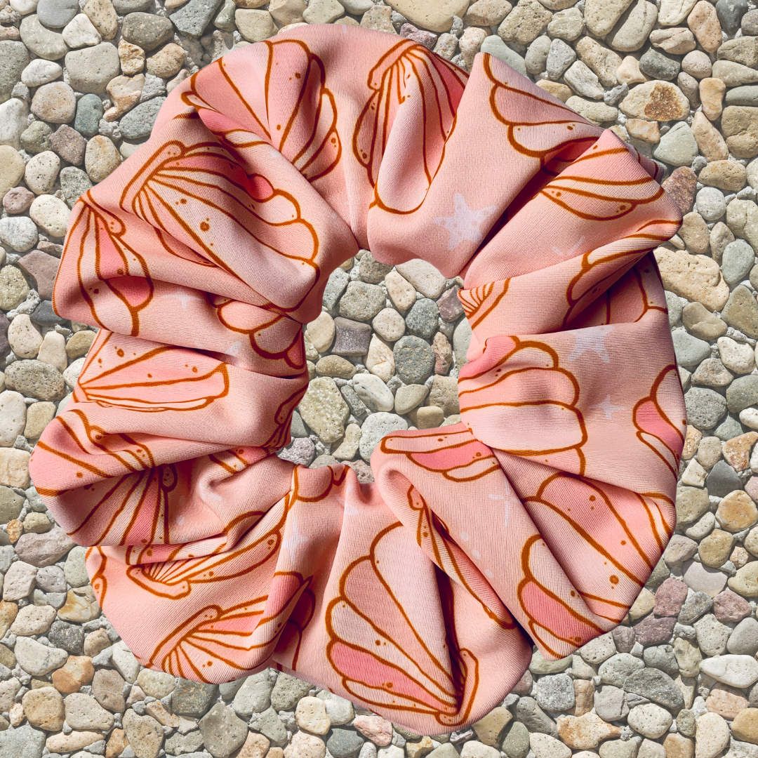 Pink swim scrunchie with shell pattern on a pebble surface