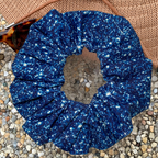 Blue printed sparkle swim scrunchie on a textured surface with hat and sunglasses