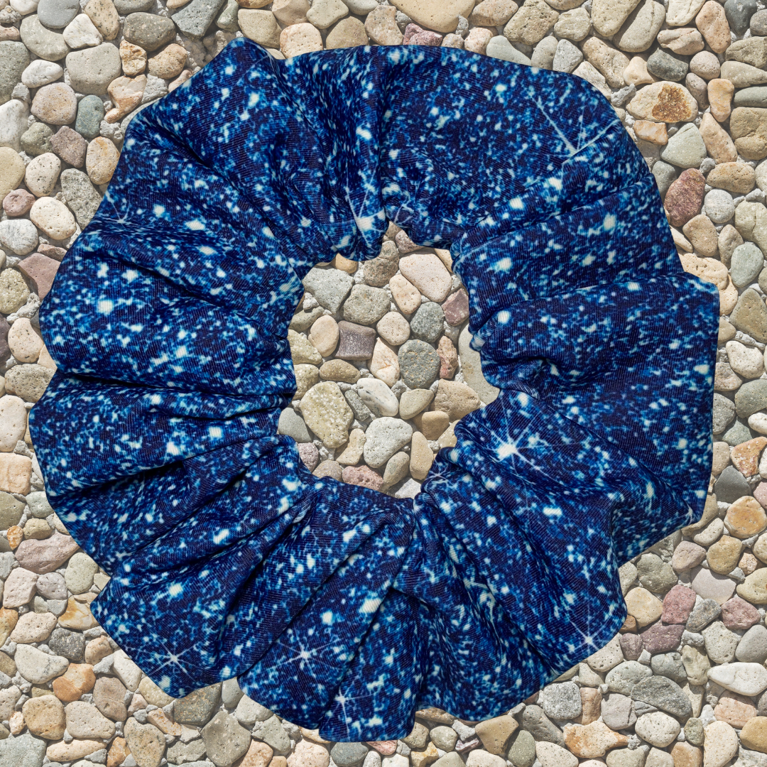 Blue printed sparkle swim scrunchie on a pebble surface