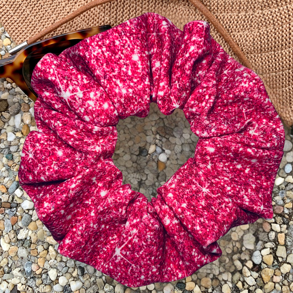 Pink printed sparkle swim scrunchie on a textured surface with a hat and sunglasses