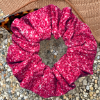 Pink printed sparkle swim scrunchie on a textured surface with a hat and sunglasses