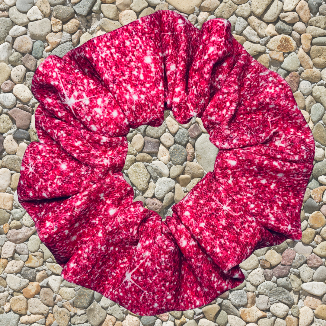 Pink printed sparkle swim scrunchie on a pebble surface