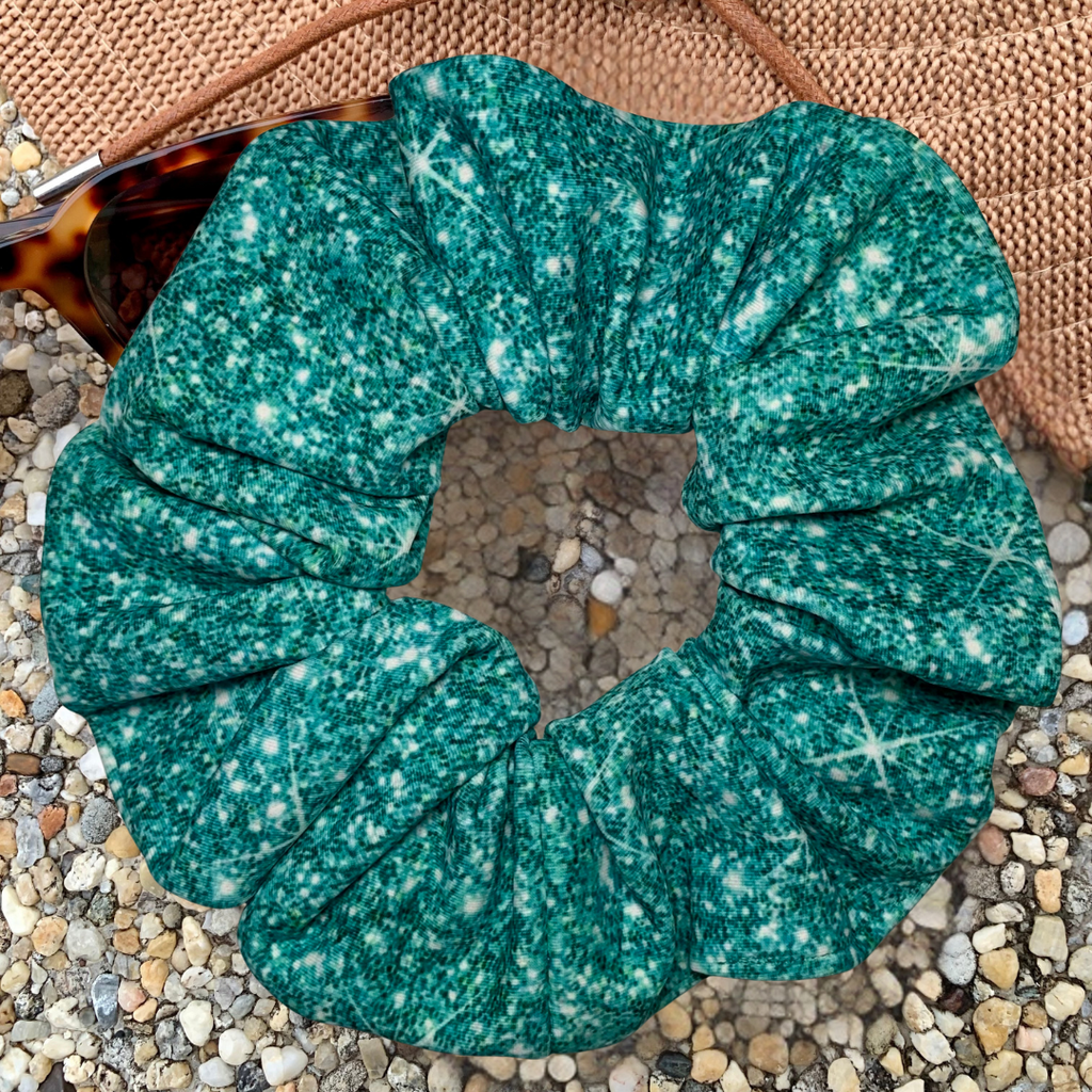 Teal printed sparkle swim scrunchie on a textured surface with hat and sunglasses