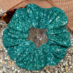 Teal printed sparkle swim scrunchie on a textured surface with hat and sunglasses
