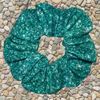 Teal printed sparkle swim scrunchie on a stone surface