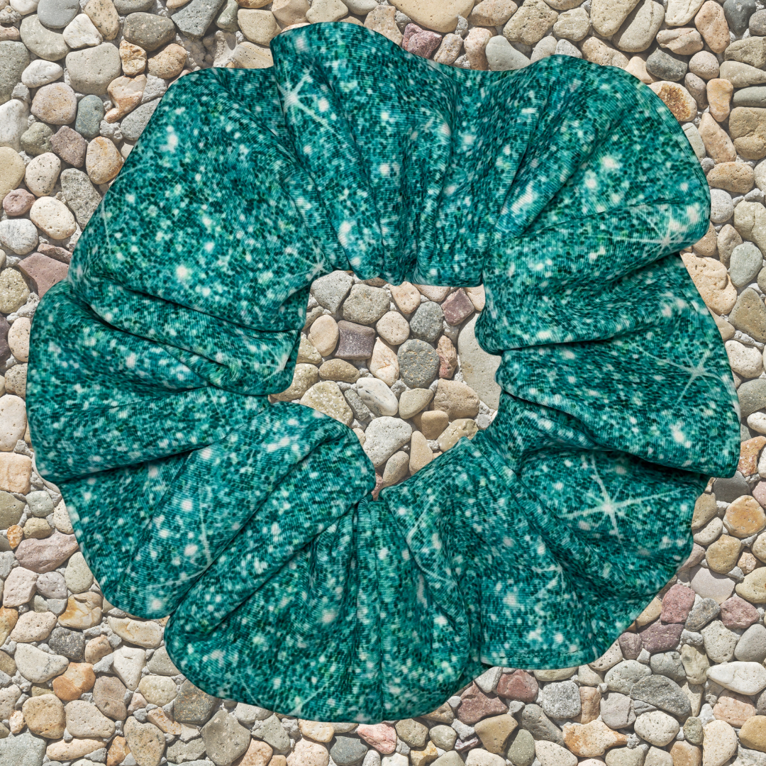 Teal printed sparkle swim scrunchie on a stone surface