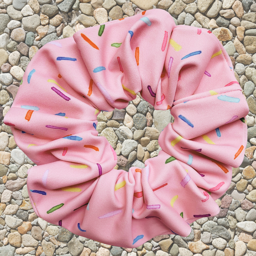 Pink swim scrunchie with colourful sprinkles on a pebbled surface