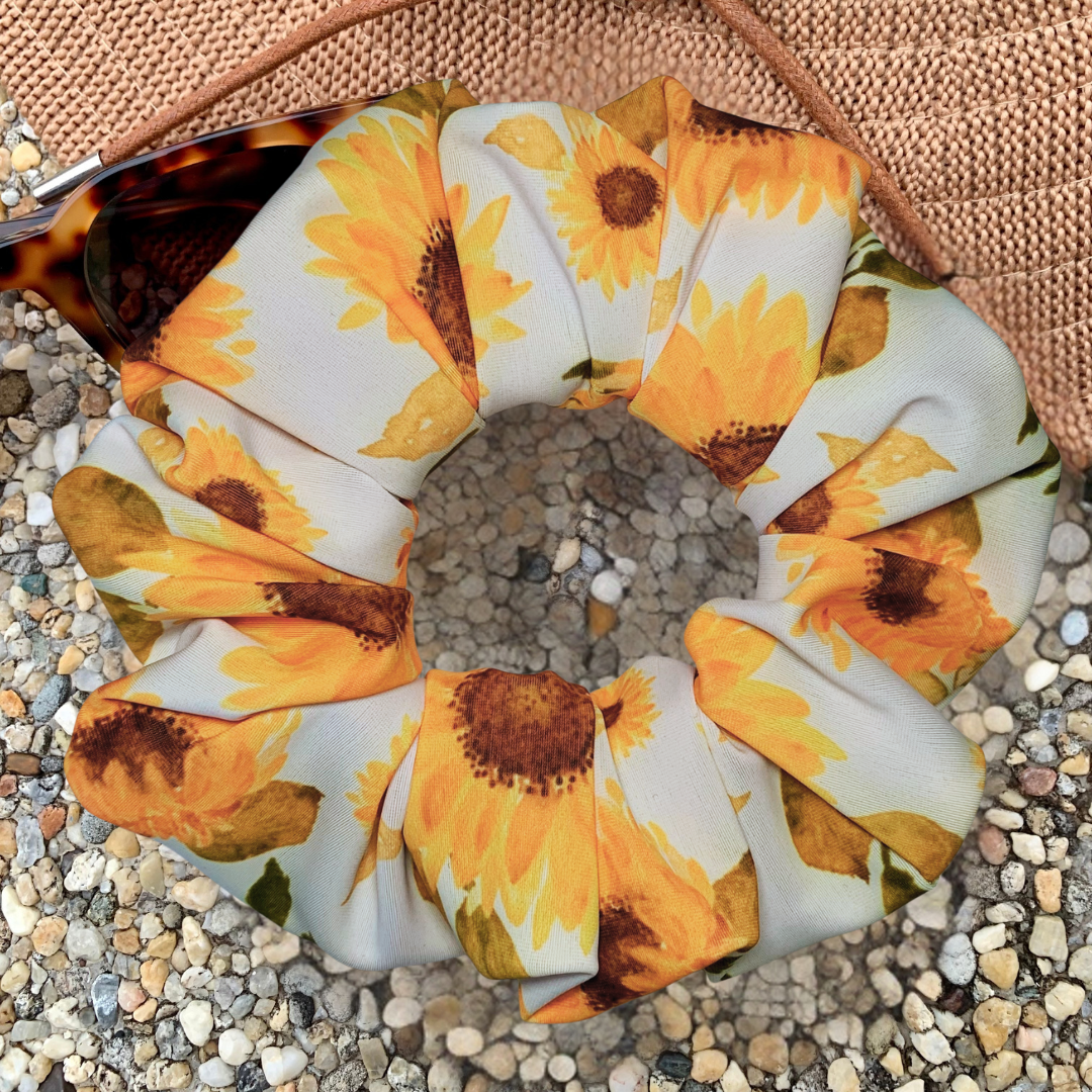 Sunflower patterned swim scrunchie on a textured surface with a hat and sunglasses